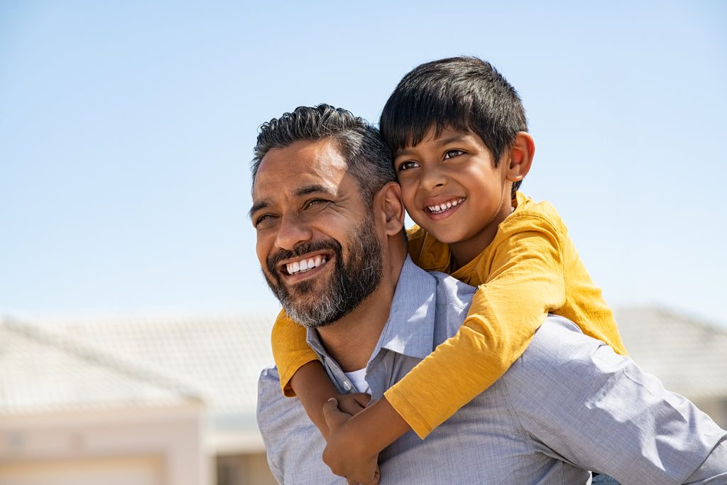 Man giving a piggyback ride to a child with a clear blue sky in the background