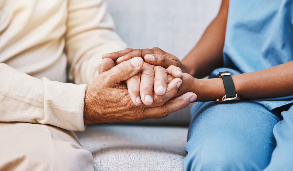 Close-up of an elderly person's hand being held by a younger person in a medical setting.